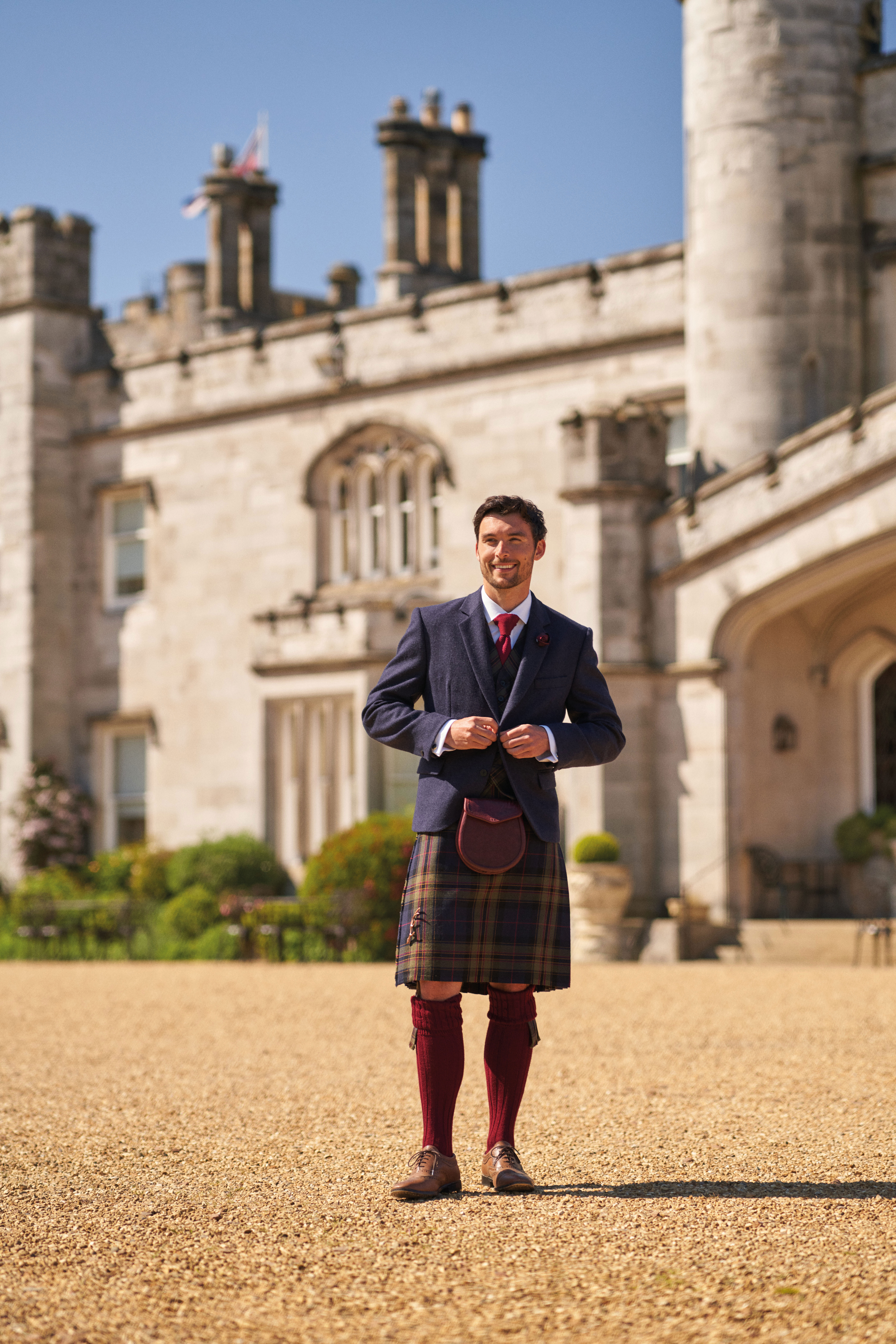 groom smiles as he fastens up his navy jacket paired with mccalls highlandwear's new noble print tartan kilt