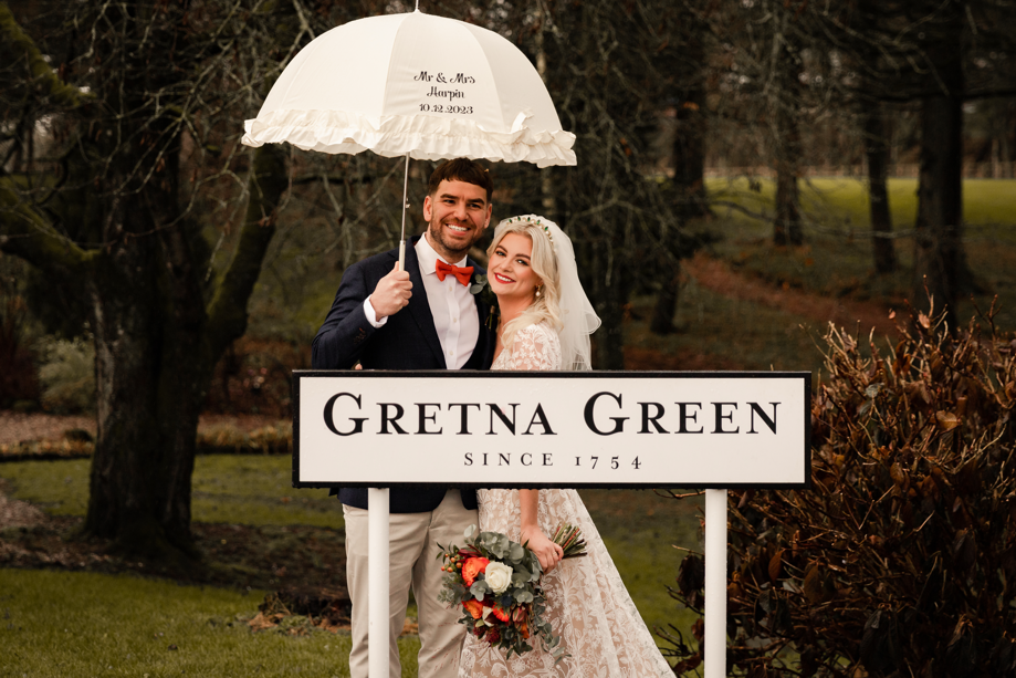 bride and groom stand next to gretna green sign after getting married