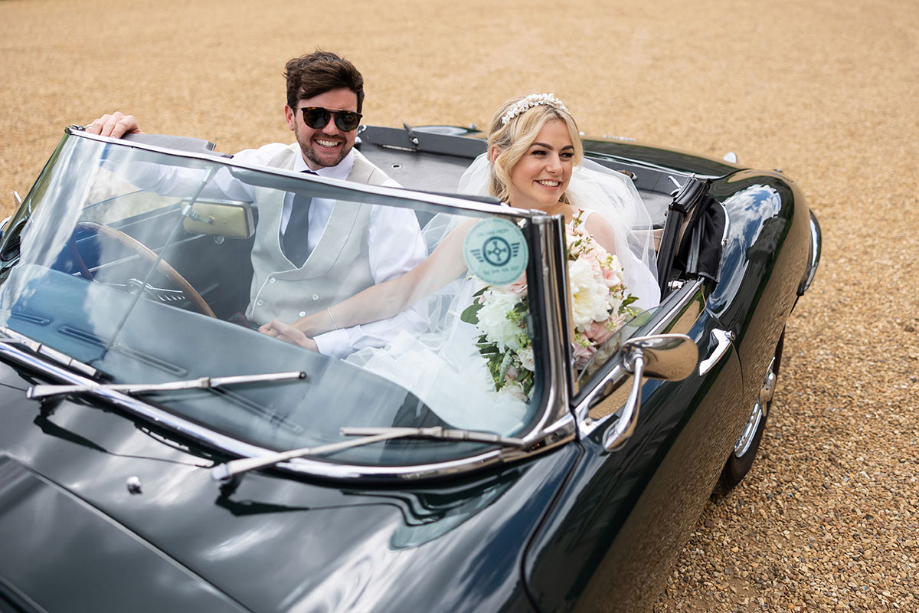 Bride and groom smile from car with convertible roof