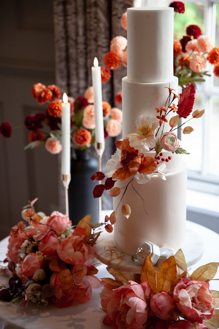 close up image of a white iced three tier wedding cake decorated with bunches of pink, orange and red flowers