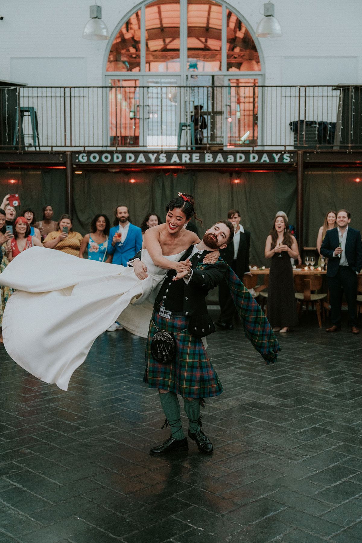 Groom lifting bride during first dance at Barras Art and Design Glasgow with guests watching