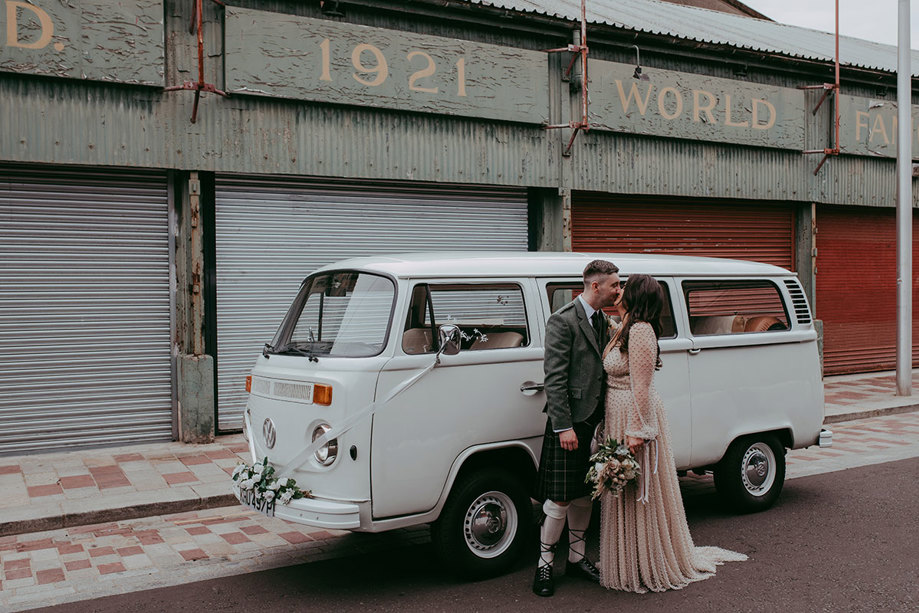 Bride and groom kiss while standing in front of VW Campervan