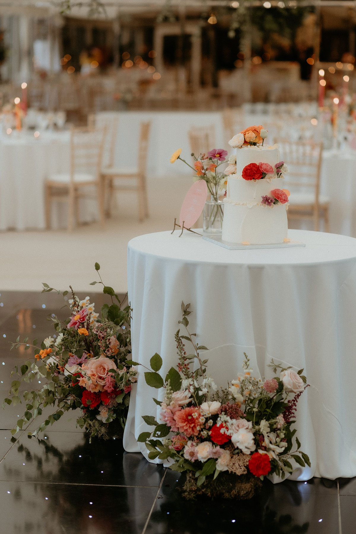 a wedding cake on a table with flower arrangements on the floor