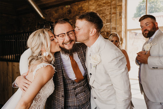 Bride and groom kissing man on cheek