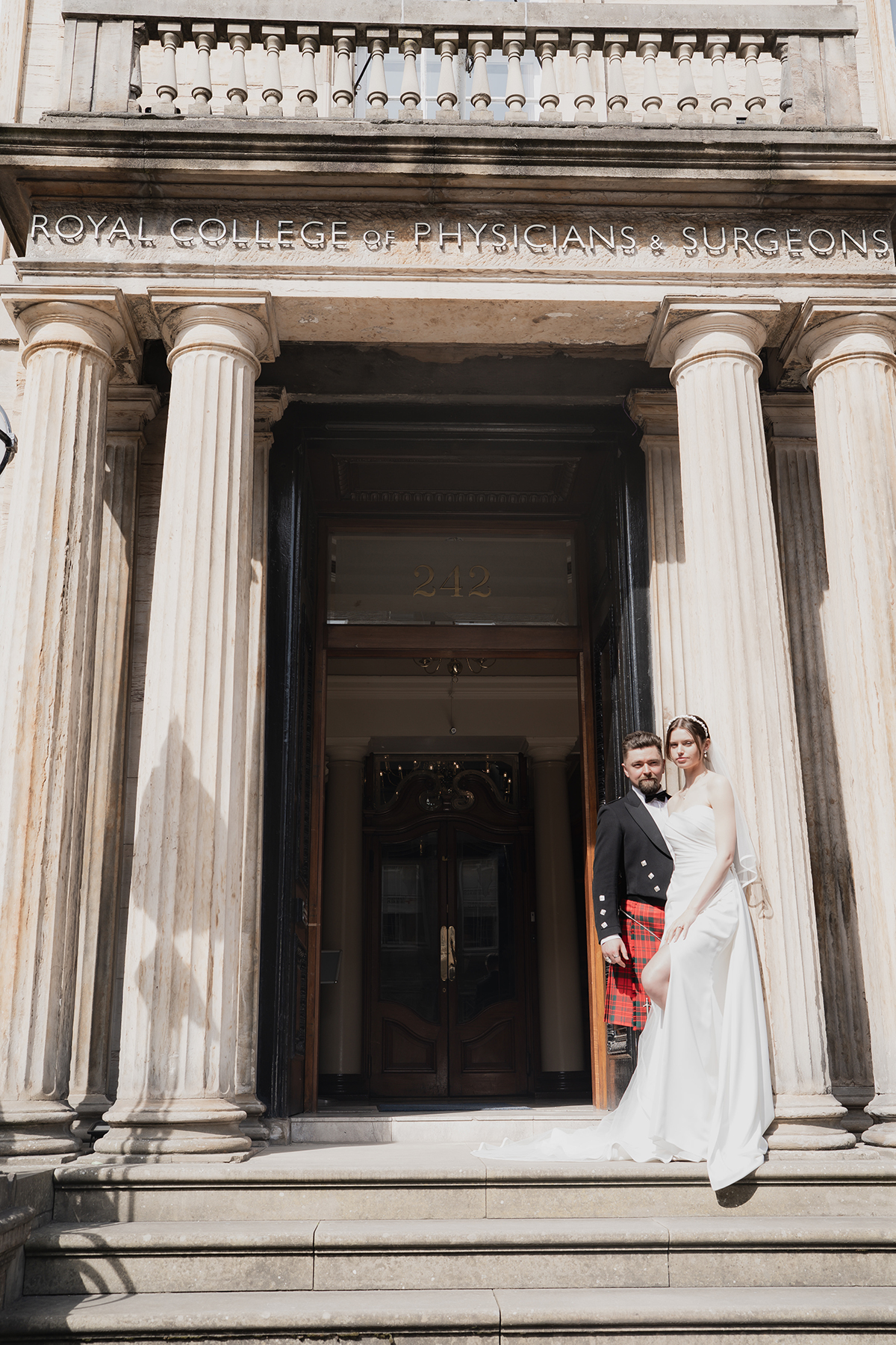 Bride and groom at entrance of Royal College of Physicians and Surgeons Edinburgh with columned facade and city backdrop