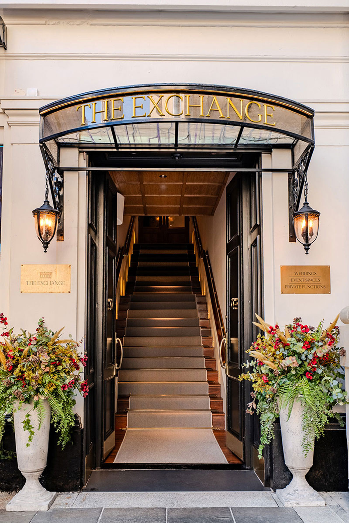front door to the exchange in glasgow with black roof and carpeted stairs with large floral arrangements at each side