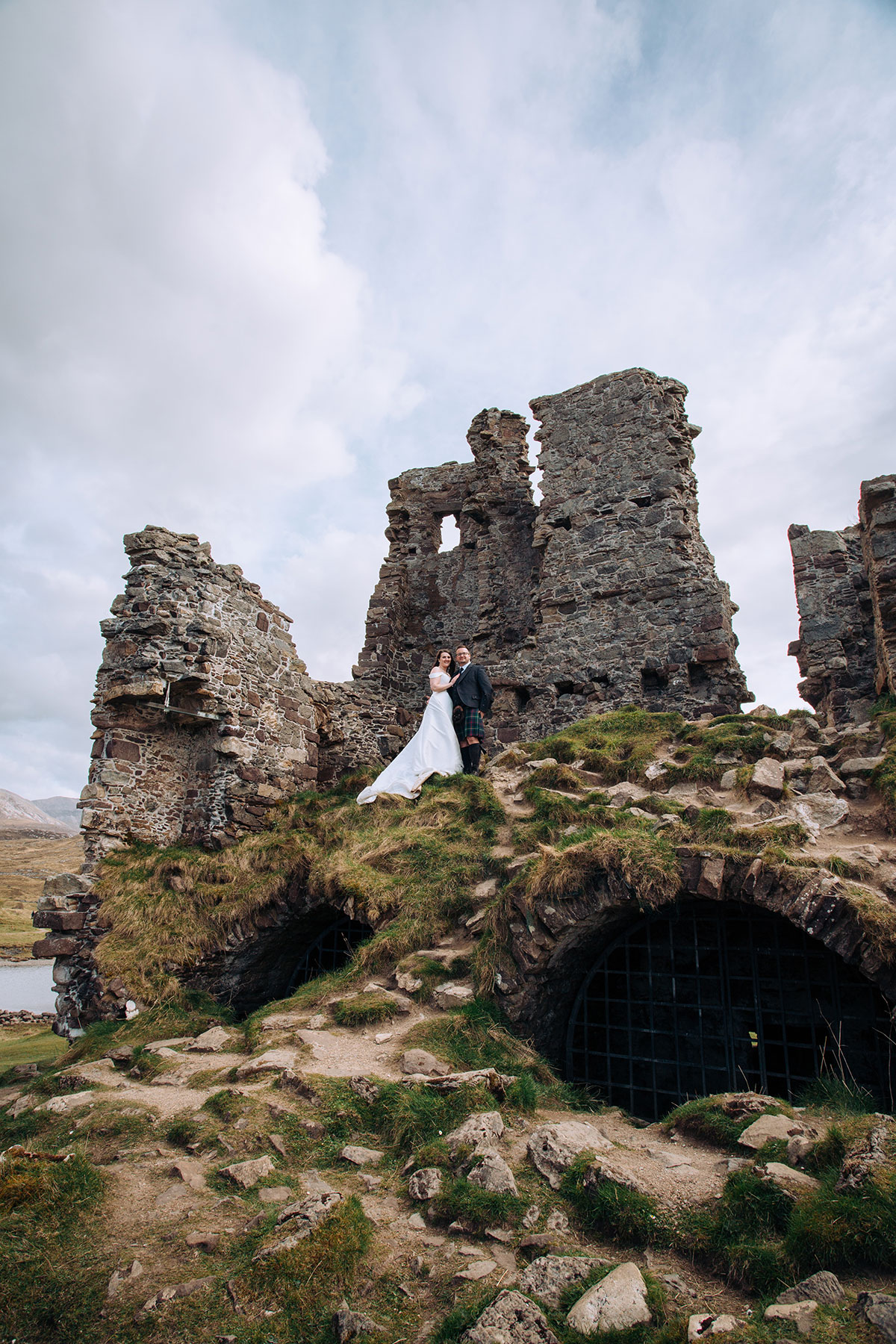 Bride and groom stand among the ruins of Ardvreck Castle for post-ceremony wedding portraits overlooking Loch Assynt.