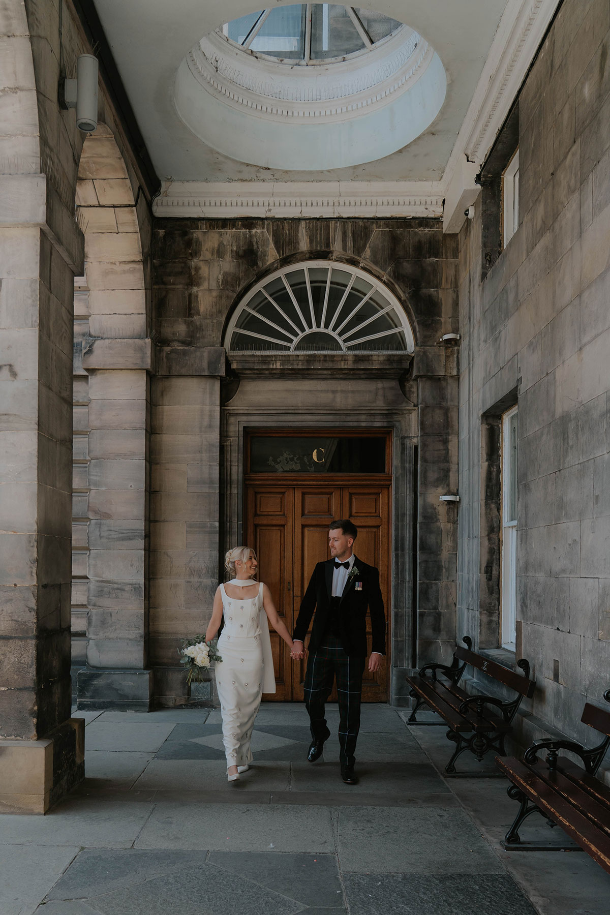 Bride and groom walking hand in hand beneath the historic stone architecture of Edinburgh City Chambers