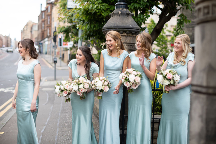 Bridesmaids wearing blue dresses smile outside venue