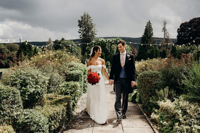 a bride and groom walking hand in hand along a path in the garden at Achnagairn Castle