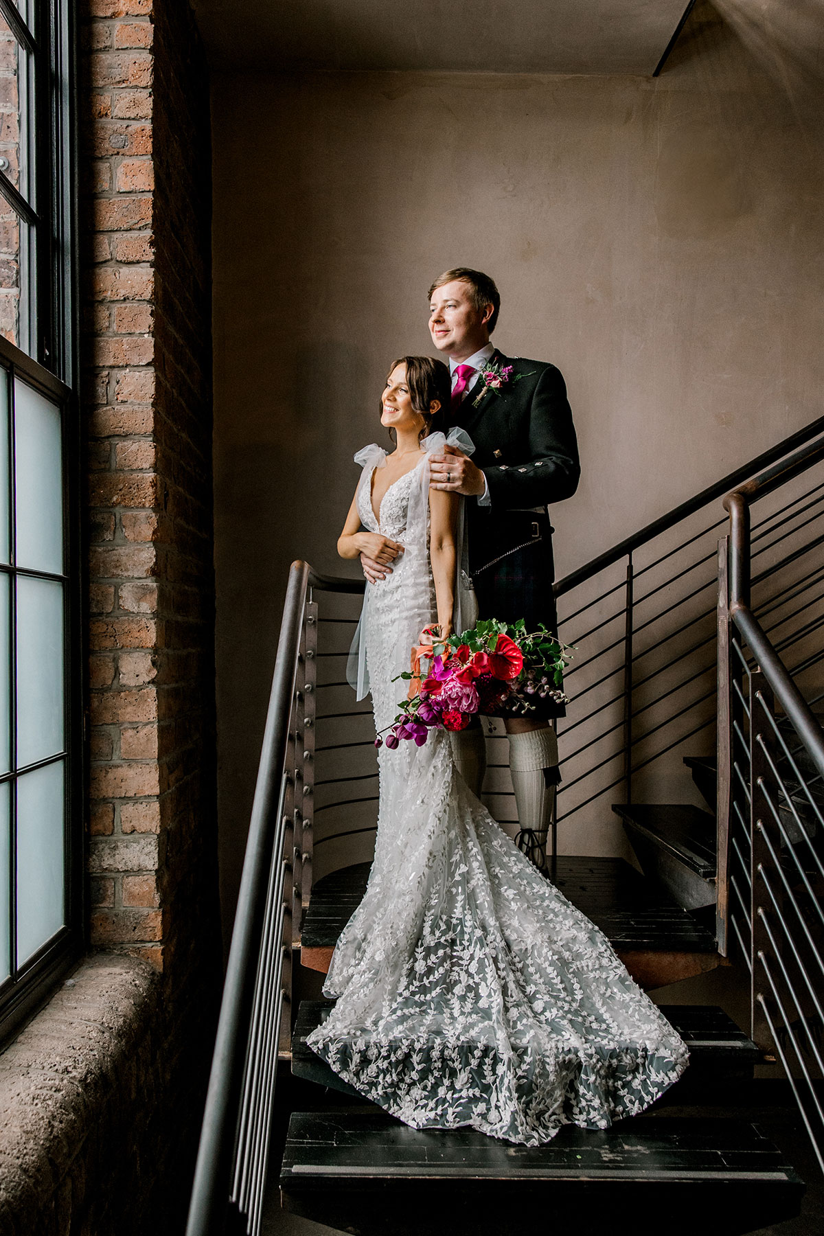 Bride and groom posing together on an industrial staircase inside their wedding venue