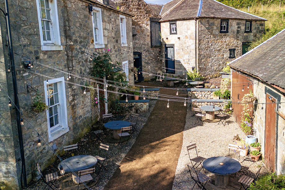 An outdoor courtyard area between two stone buildings, with festoon lights and tables and chairs