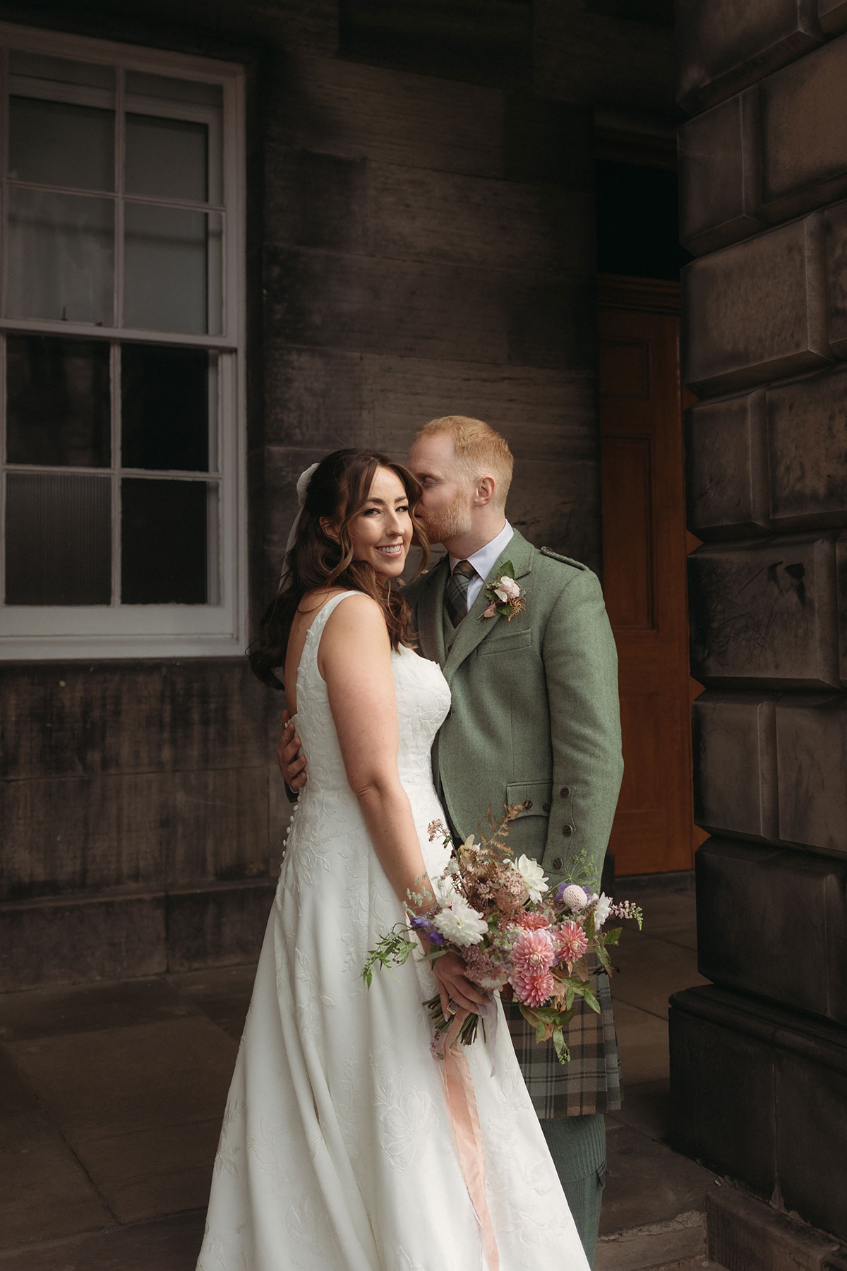 a bride and groom kissing in front of a stone building.