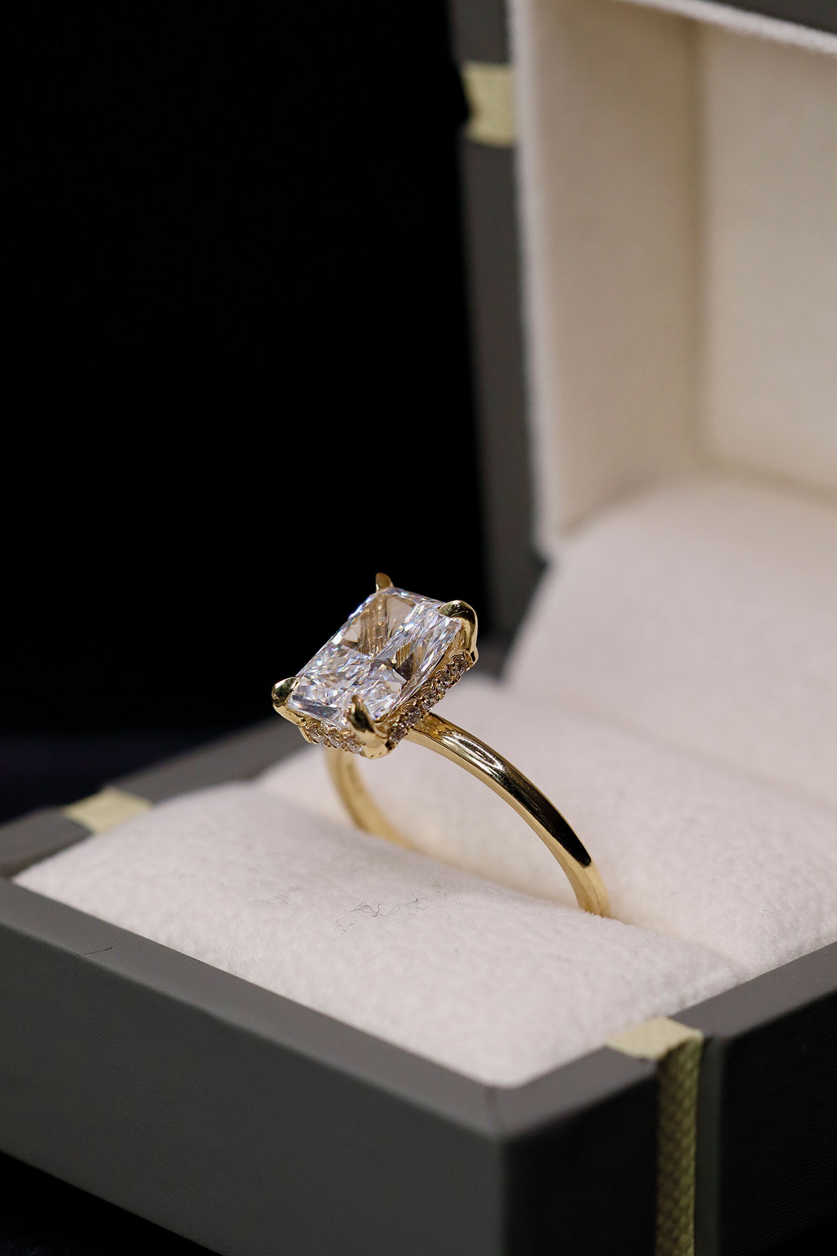 Bespoke gold engagement ring with a rectangular centre stone displayed in a ring box by John Stewart Jewellers
