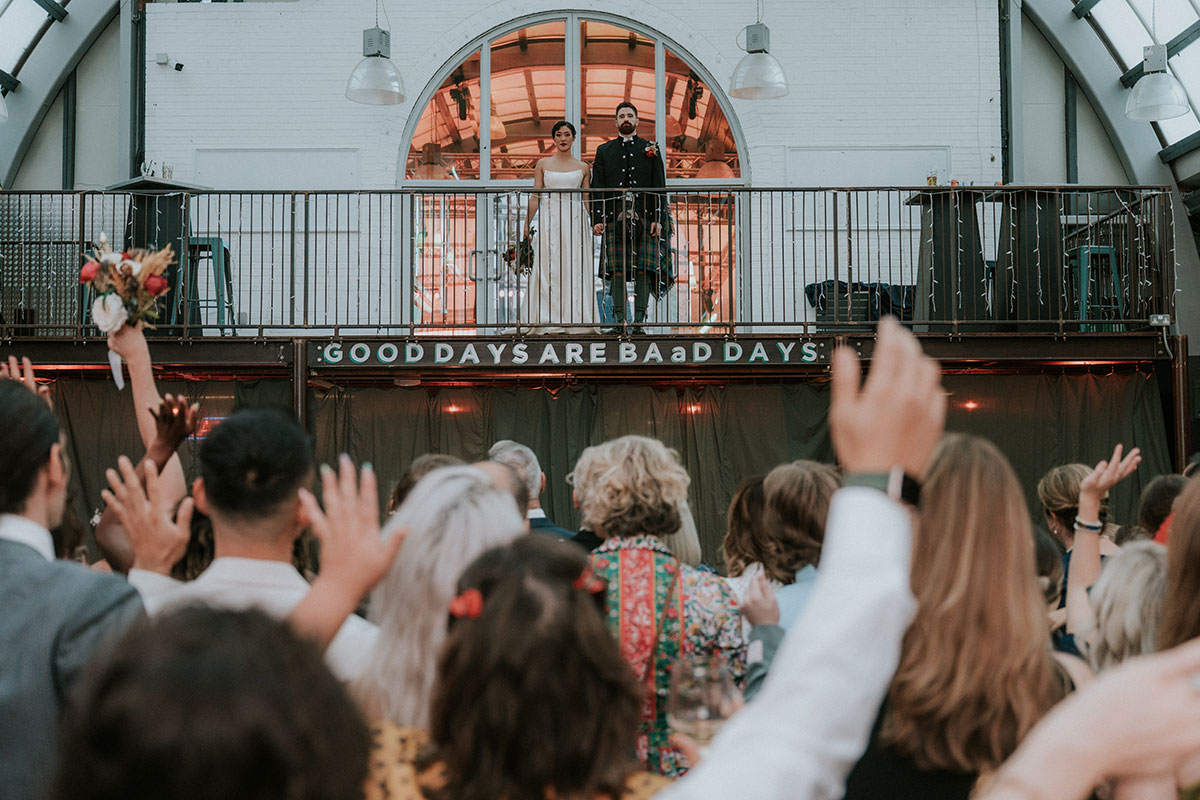 Bride and groom standing on balcony at BAaD Glasgow greeting guests below during wedding reception