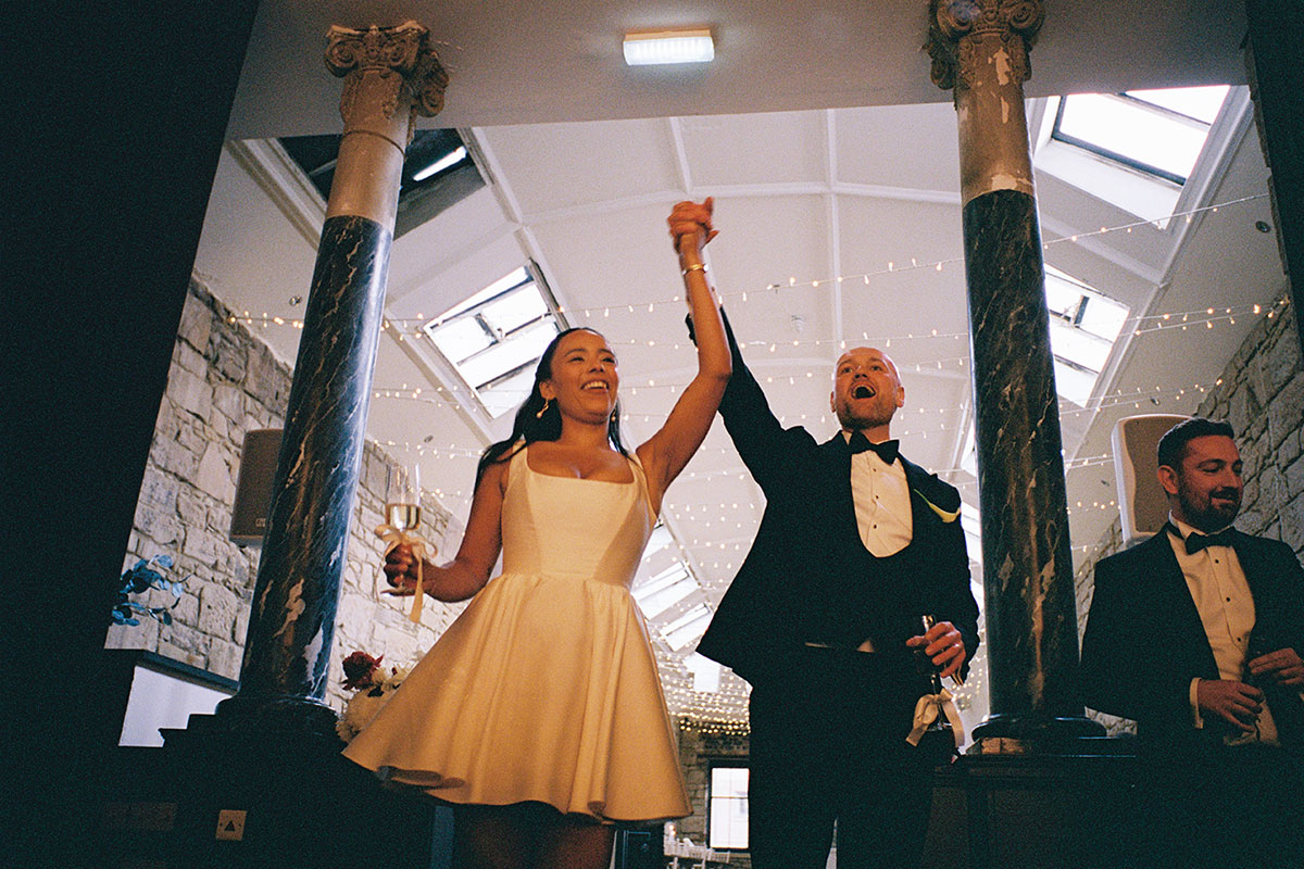 Bride and groom entering The Haberdashery Glasgow wedding reception cheering with guests under festoon lights