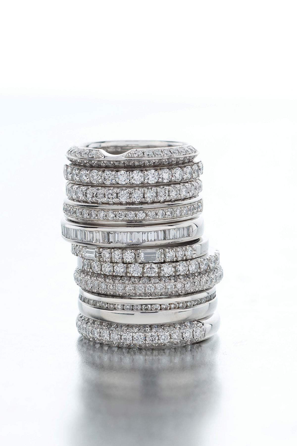 a stack of eleven different white gold and platinum diamond wedding bands with a plain white background