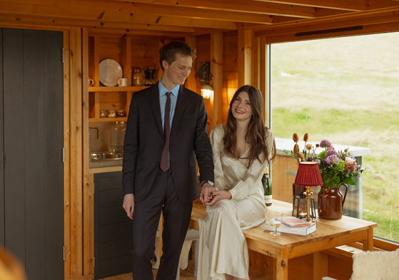 bride sits on wooden table as groom wearing a navy suit holds her hand at guardswell farm