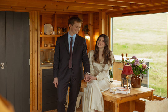 bride sits on wooden table as groom wearing a navy suit holds her hand at guardswell farm