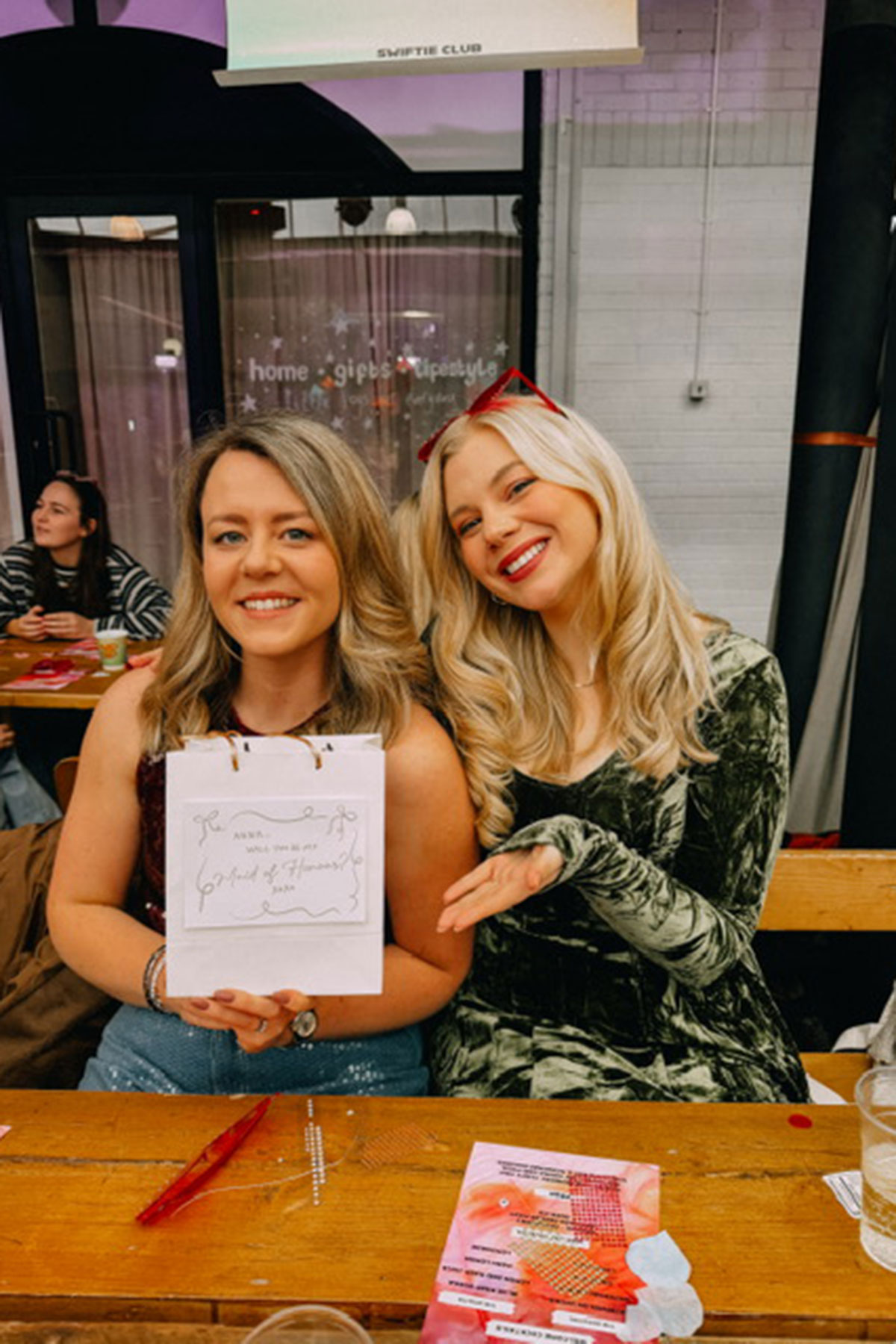 Two women seated at table smiling with gift bag at social event or workshop