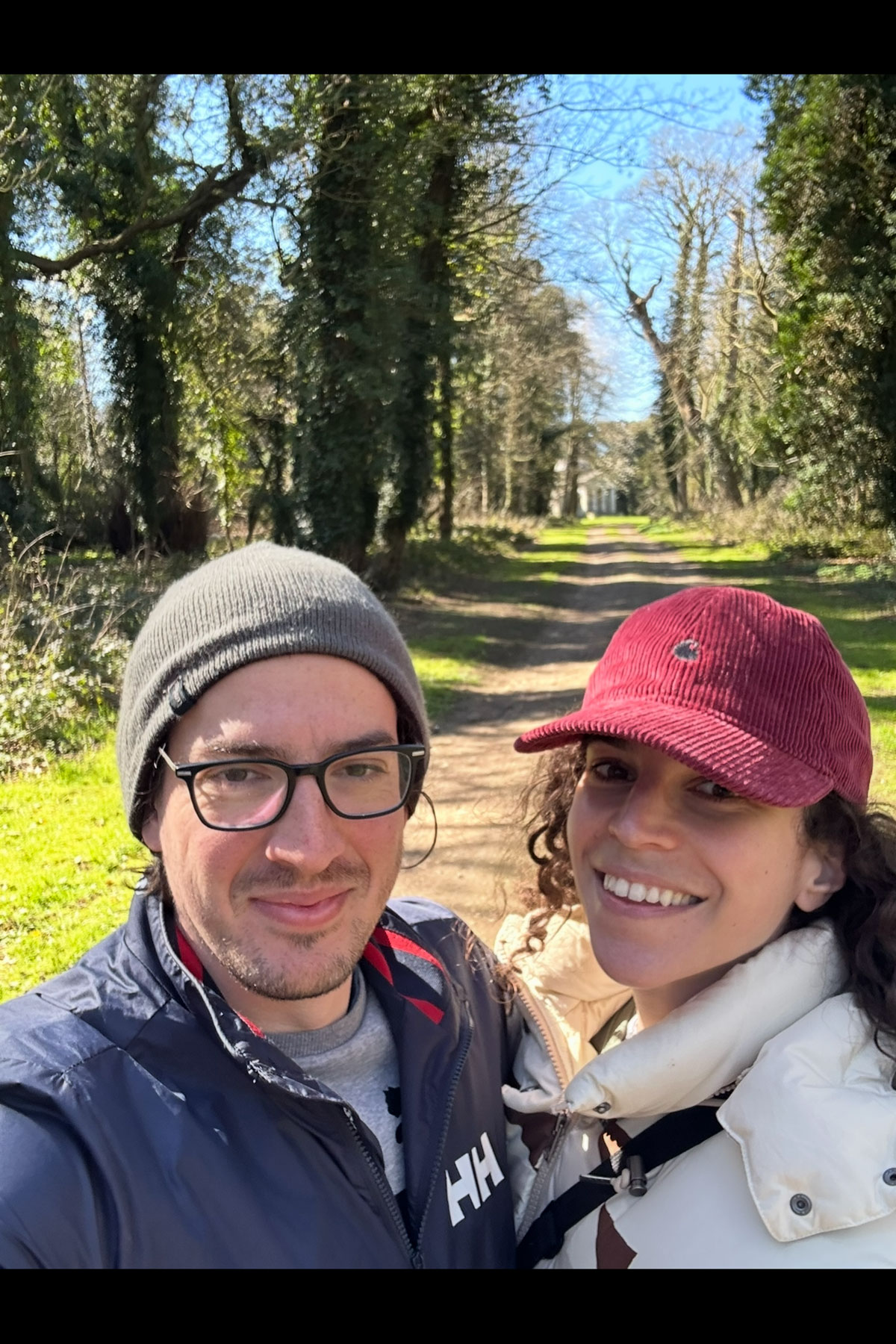 Couple smiling during a countryside walk on a tree-lined avenue before their Scottish wedding celebration