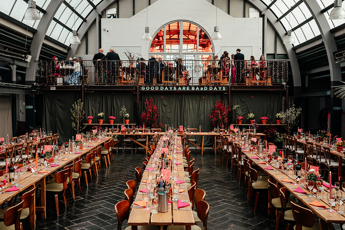 Wedding breakfast set-up inside BAaD Glasgow with long wooden tables, colourful décor and mezzanine seating above.