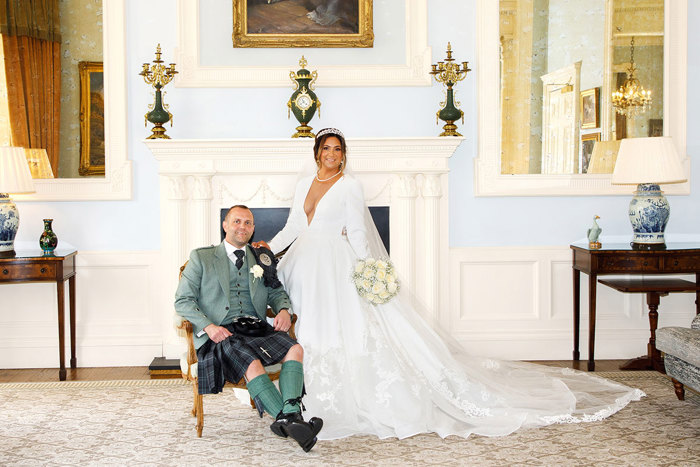 a bride and groom posing by a fireplace in an elegant room