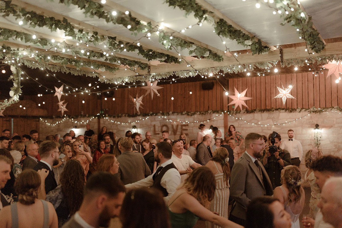Evening wedding reception at Eden Leisure Village with guests dancing under fairy lights and greenery in the rustic barn.