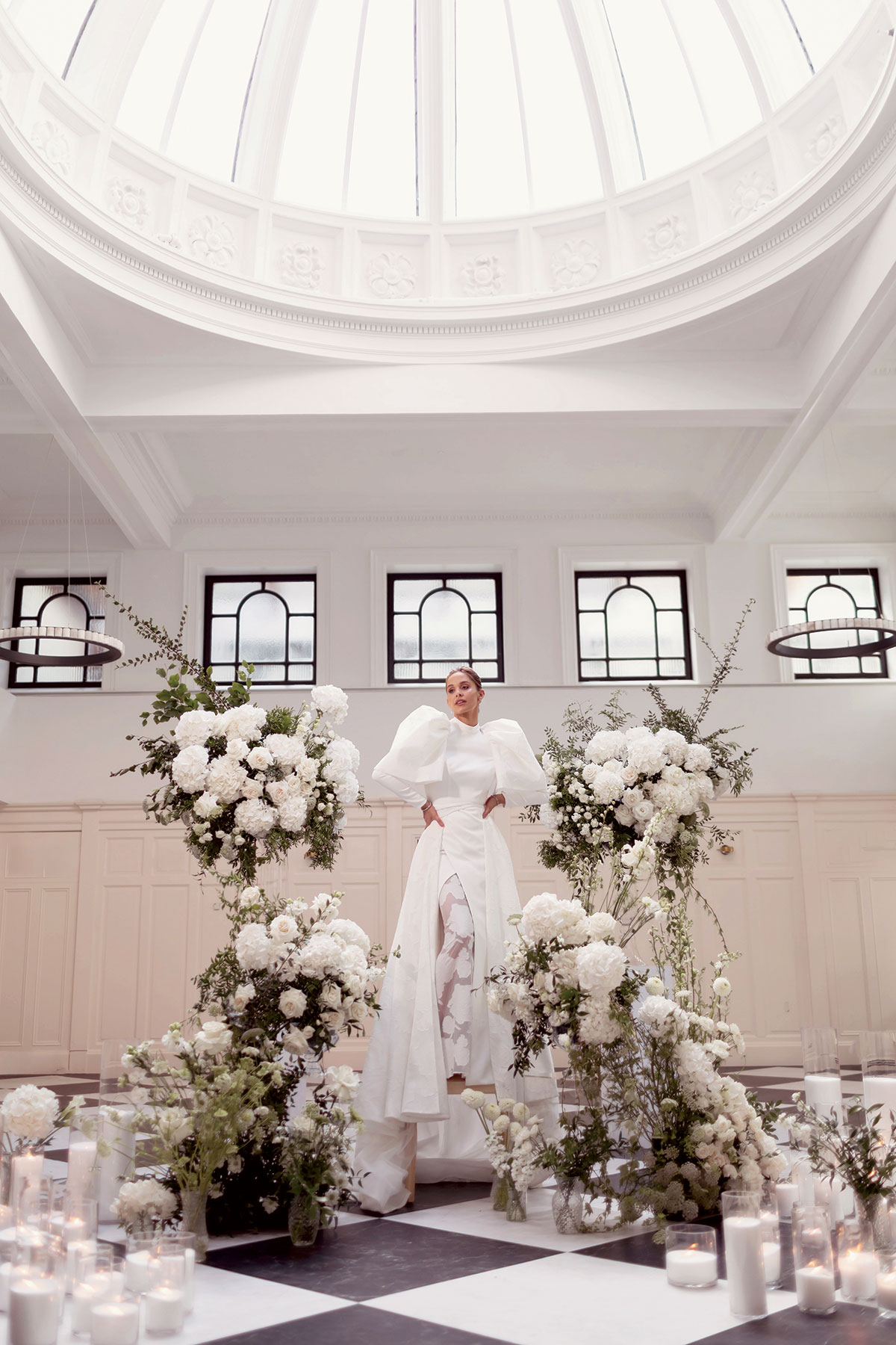 emily shak wearing a wedding dress while standing on a chair and surrounded by flowers at the collector's hall in glasgow
