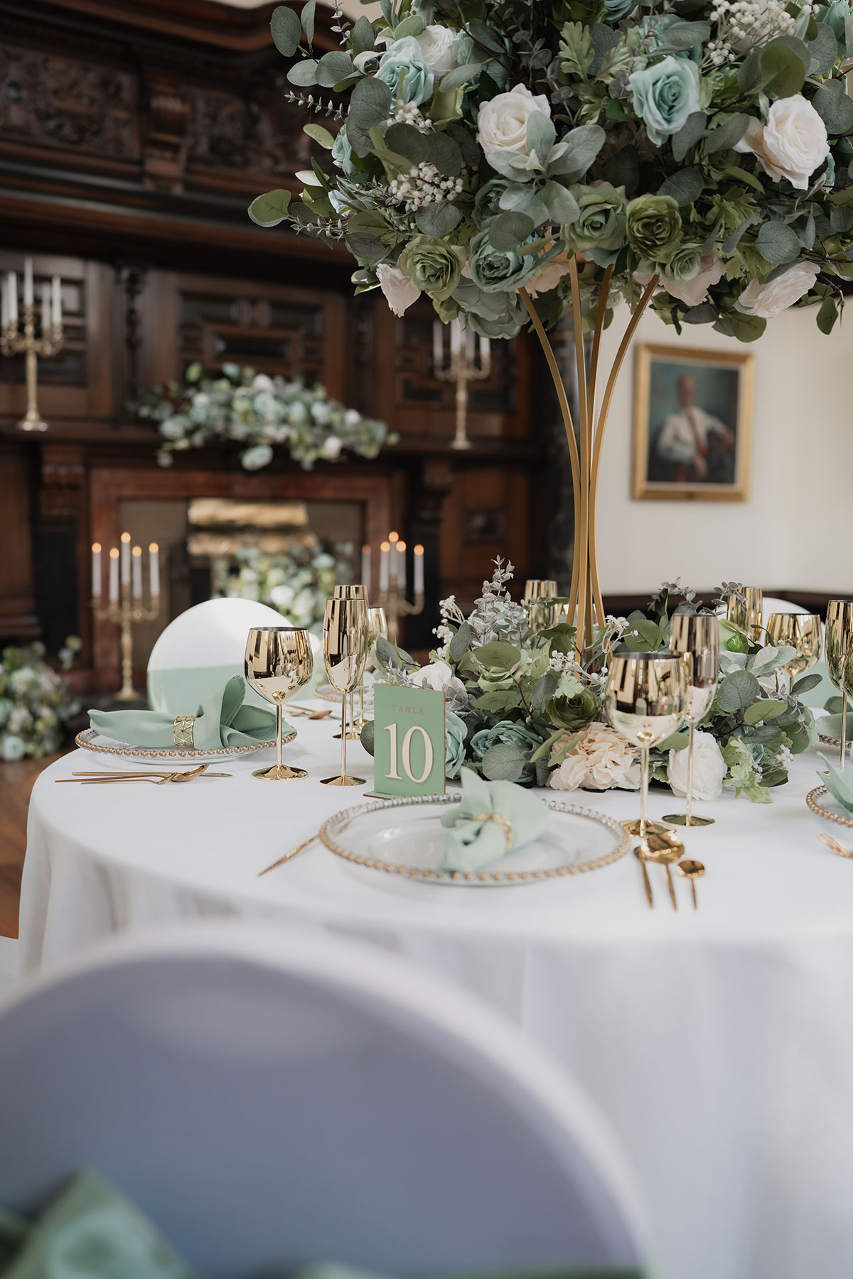 Elegant wedding table styling with tall green and white floral centrepiece, gold glassware and mint napkins in the historic Grand Hall at 1599 at the Royal College, Edinburgh
