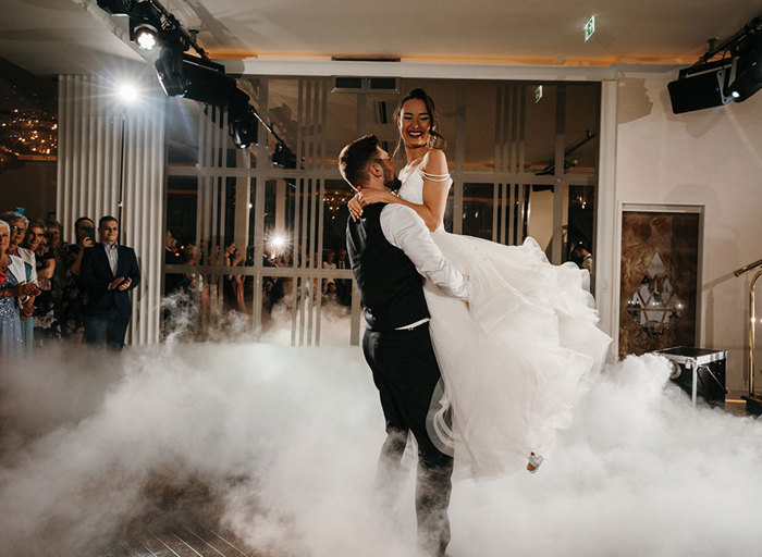 groom lifting bride on dancefloor surrounded by white smoke and onlookers watching