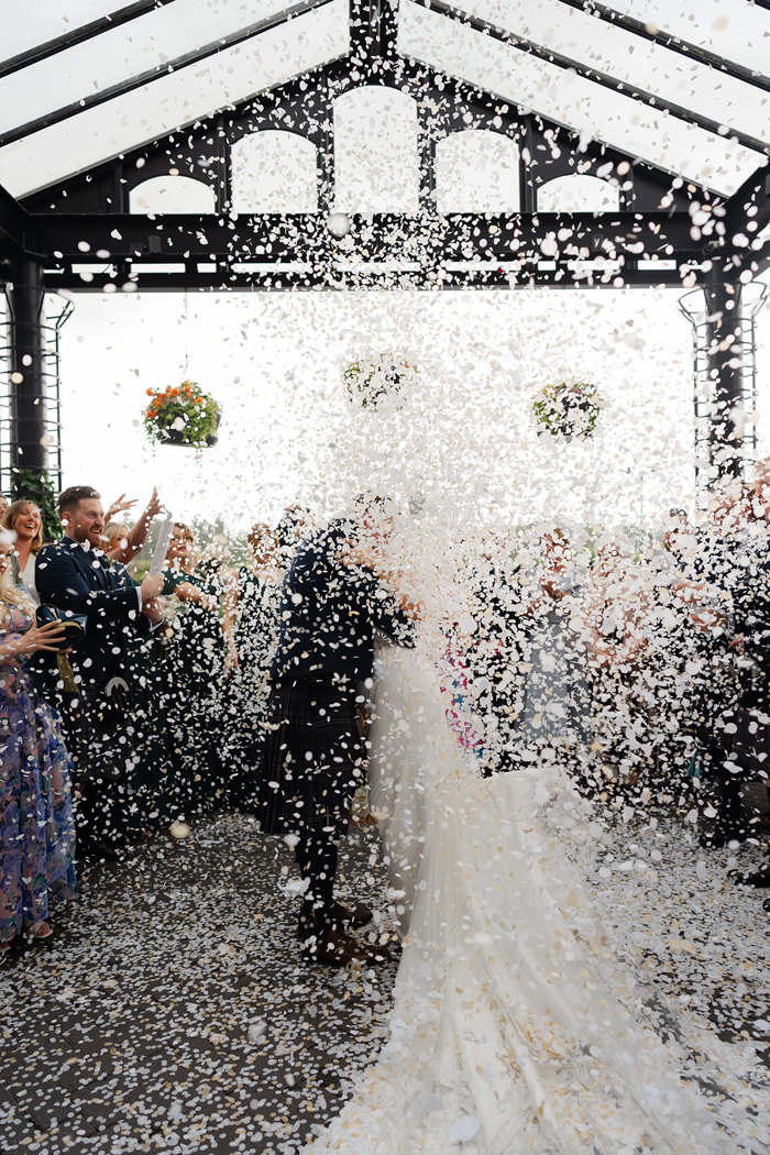 a shower of white confetti obscures a bride and groom