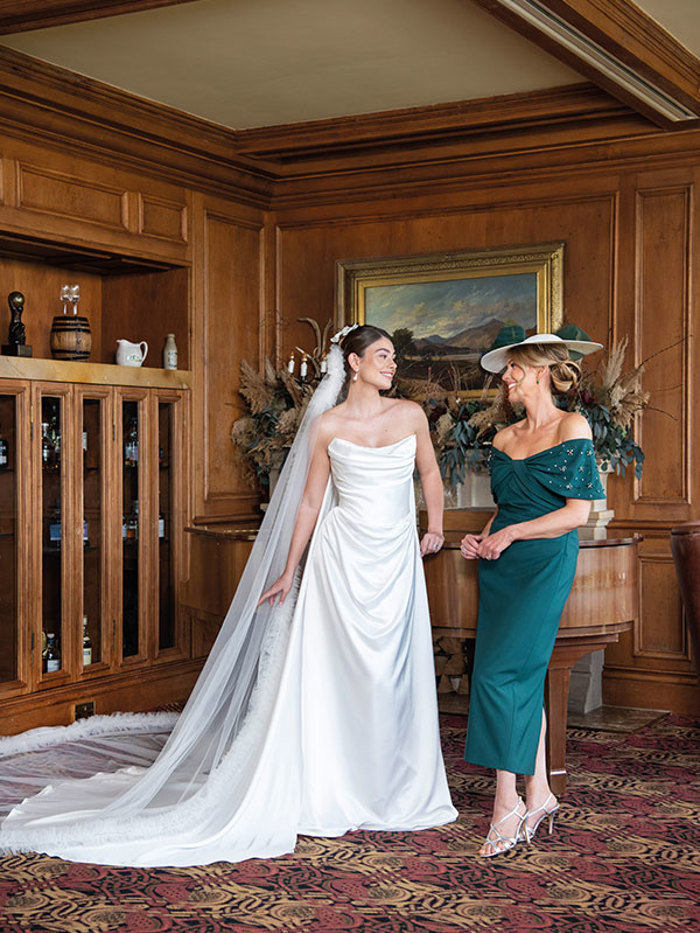 A bride wearing a strapless white wedding dress and long veil and a mother of the bride wearing forest green dress