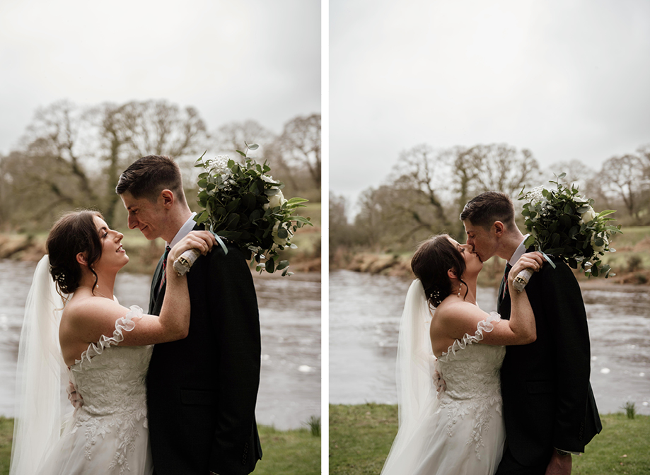 A bride and groom kiss in front of a lake