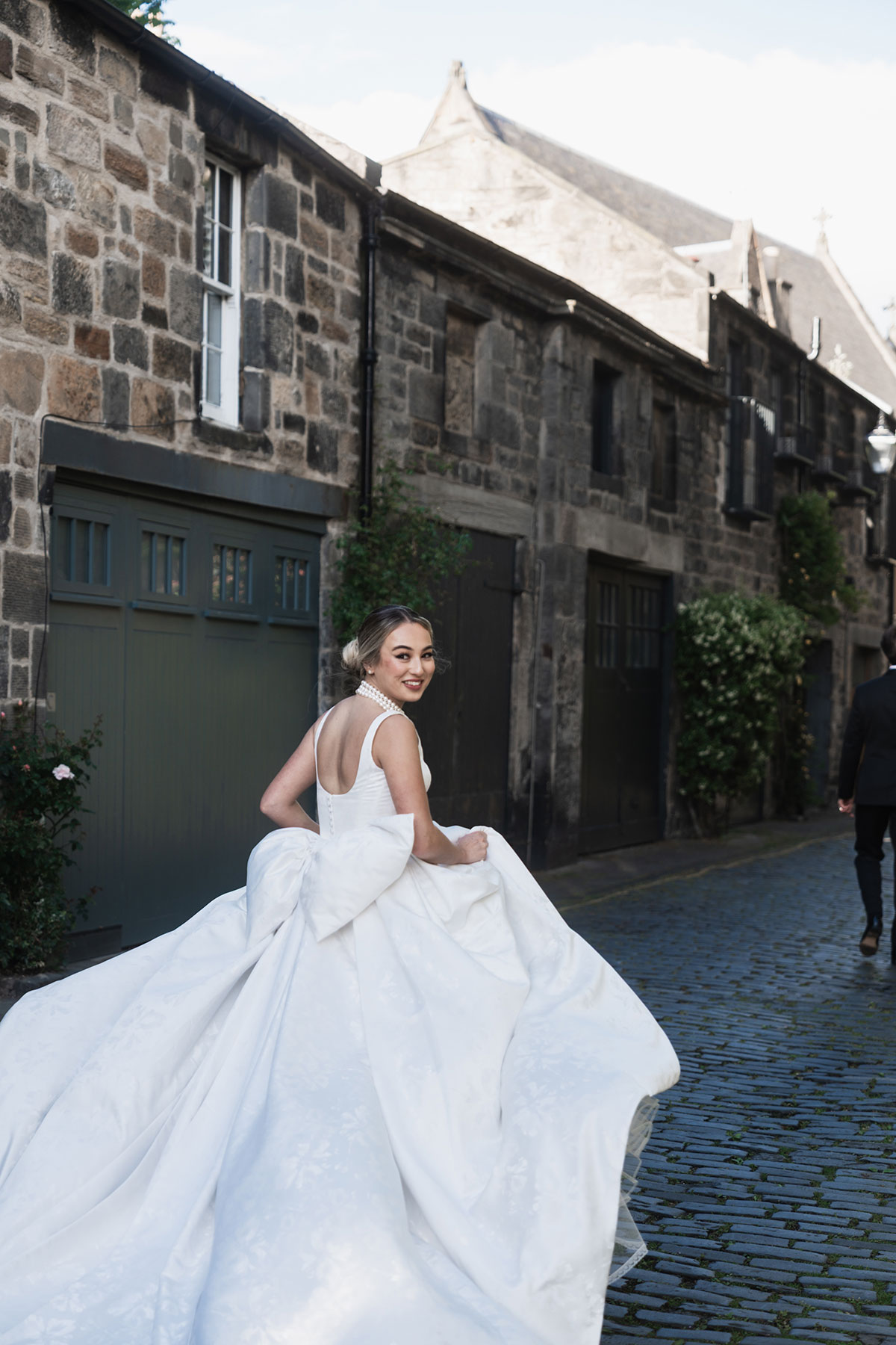 Bride posing in voluminous gown with oversized bow in Edinburgh mews street