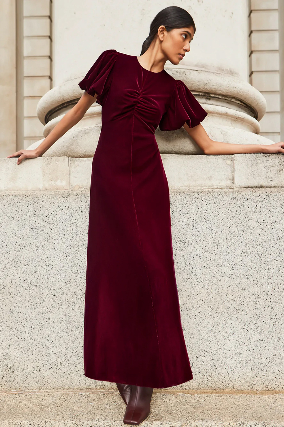 Woman wearing a burgundy velvet maxi dress with ruched detailing and statement puff sleeves.
