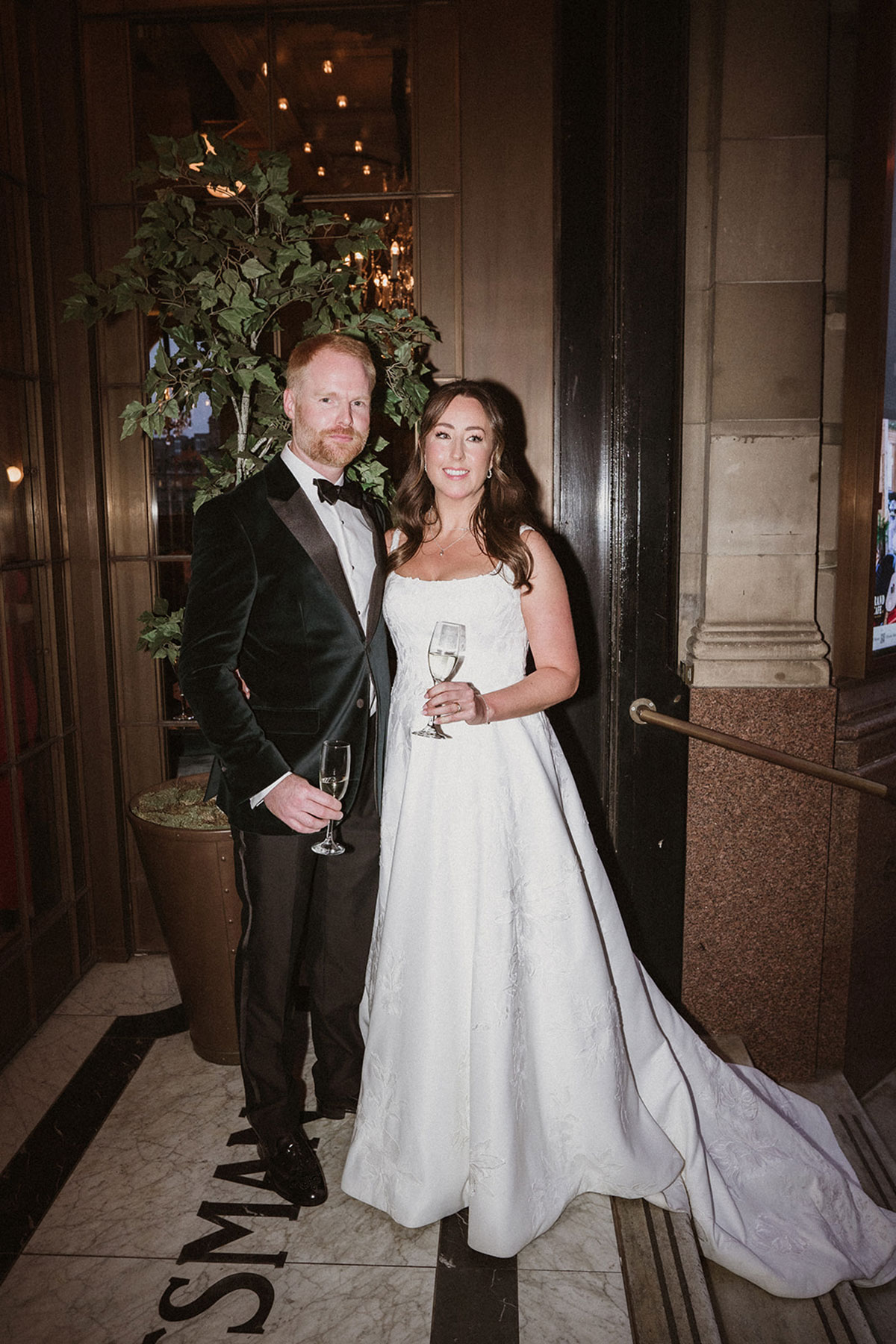 a groom wearing a velvet jacket and bride wearing square-necked wedding dress posing for a photo at the Scotsman Hotel