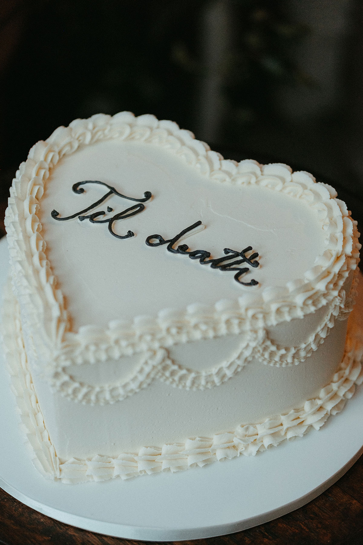 Vintage-inspired heart-shaped wedding cake with piped icing details and "Til death" script displayed at the Cambo Country House reception.