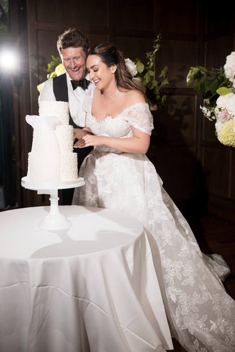 Bride and groom cutting their elegant white wedding cake during their reception at Crossbasket Castle near Glasgow.