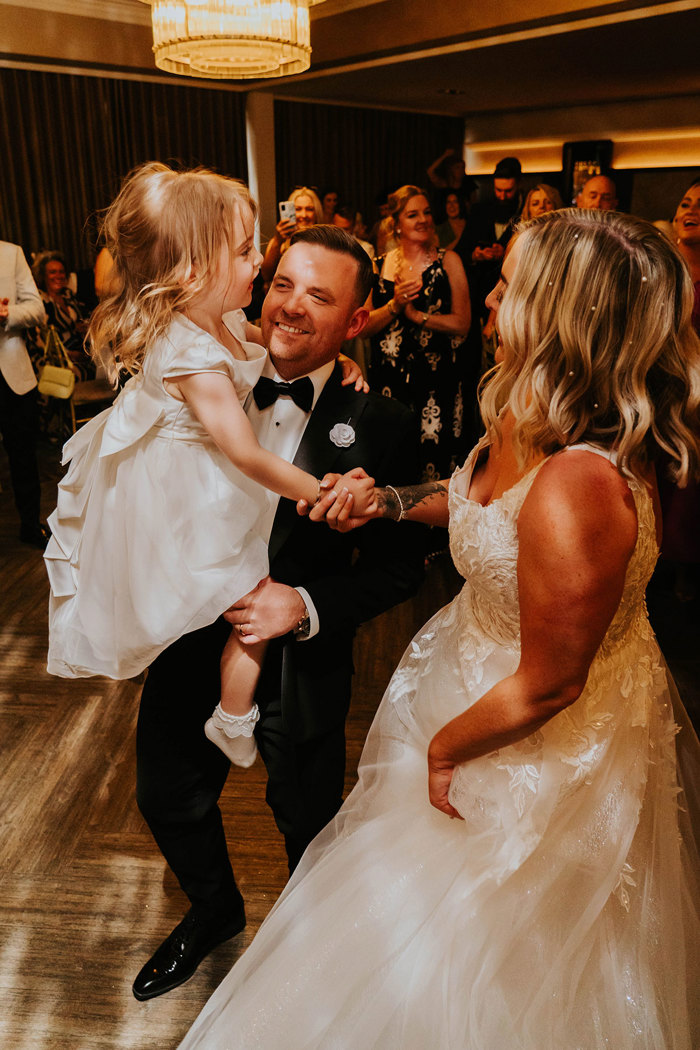 A bride and groom holding a child while on a dance floor.