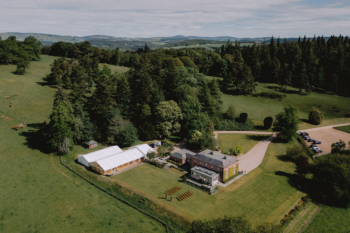 Aerial view of Ballogie House wedding venue in Aberdeenshire, with a large white marquee, extensive lawns and surrounding woodland.
