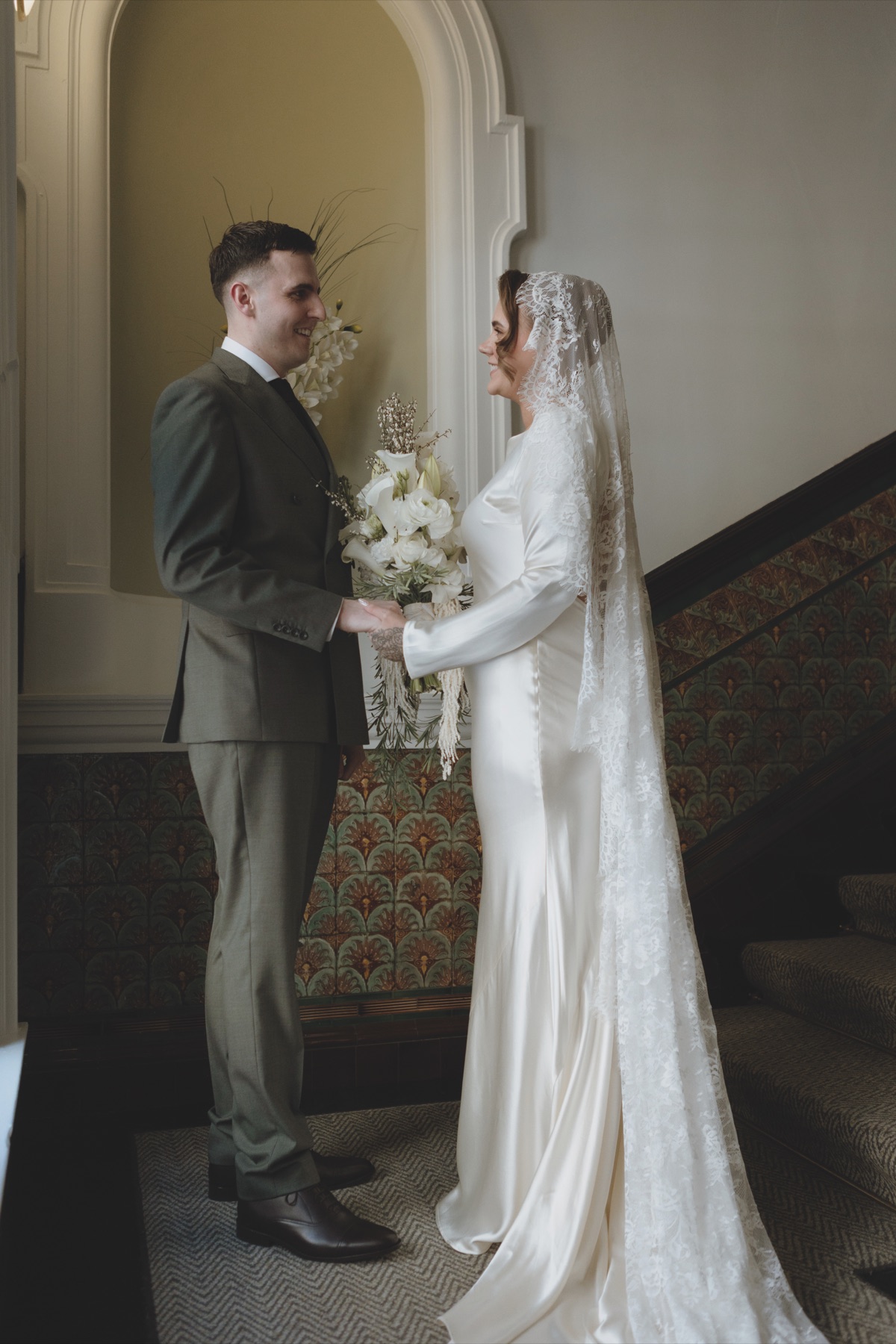 Newlyweds holding hands on a staircase at 23 Montrose Street in Glasgow, with the bride wearing a long lace veil.
