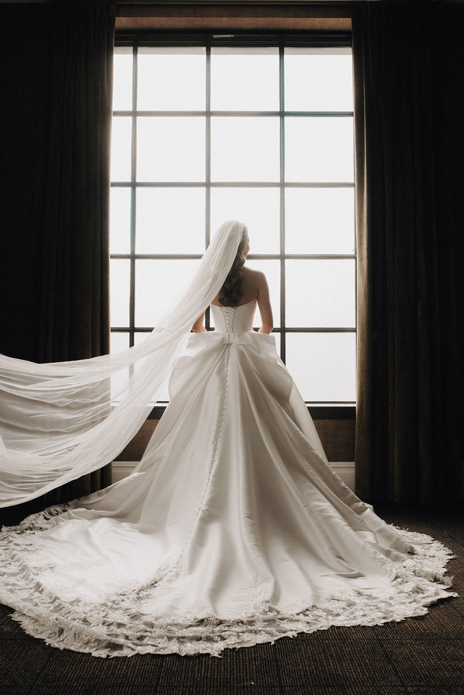 the back of a bride in a wedding dress silhouetted against a window.