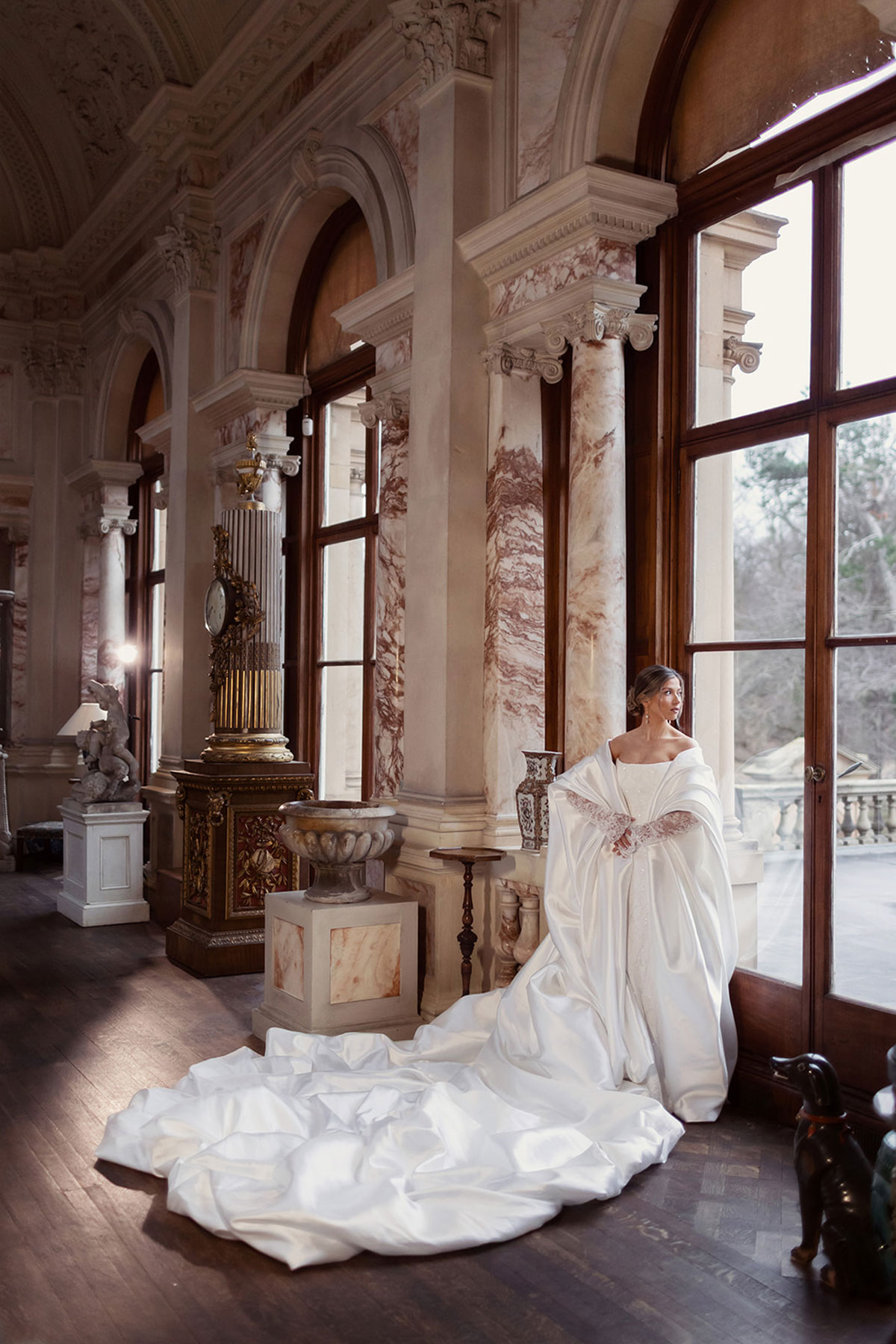 Bridal model in a satin wrap and wedding gown posed beside tall windows at Gosford House.