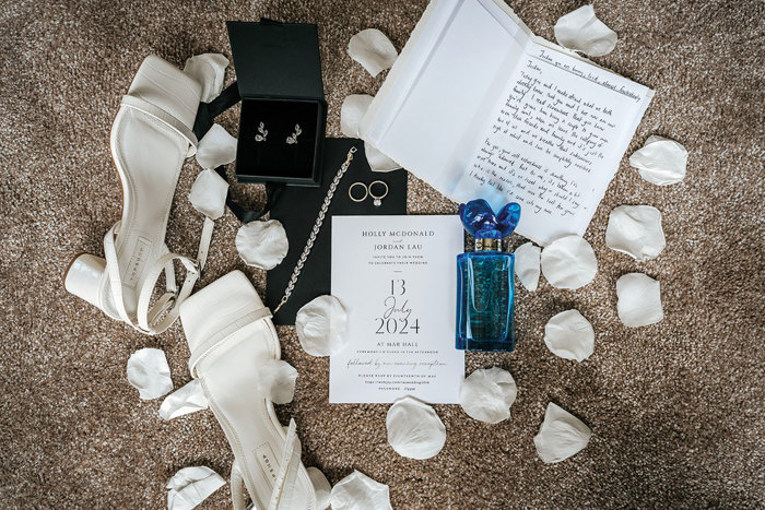 flat lay of wedding items layed out on carpet including shoes, confetti and perfume