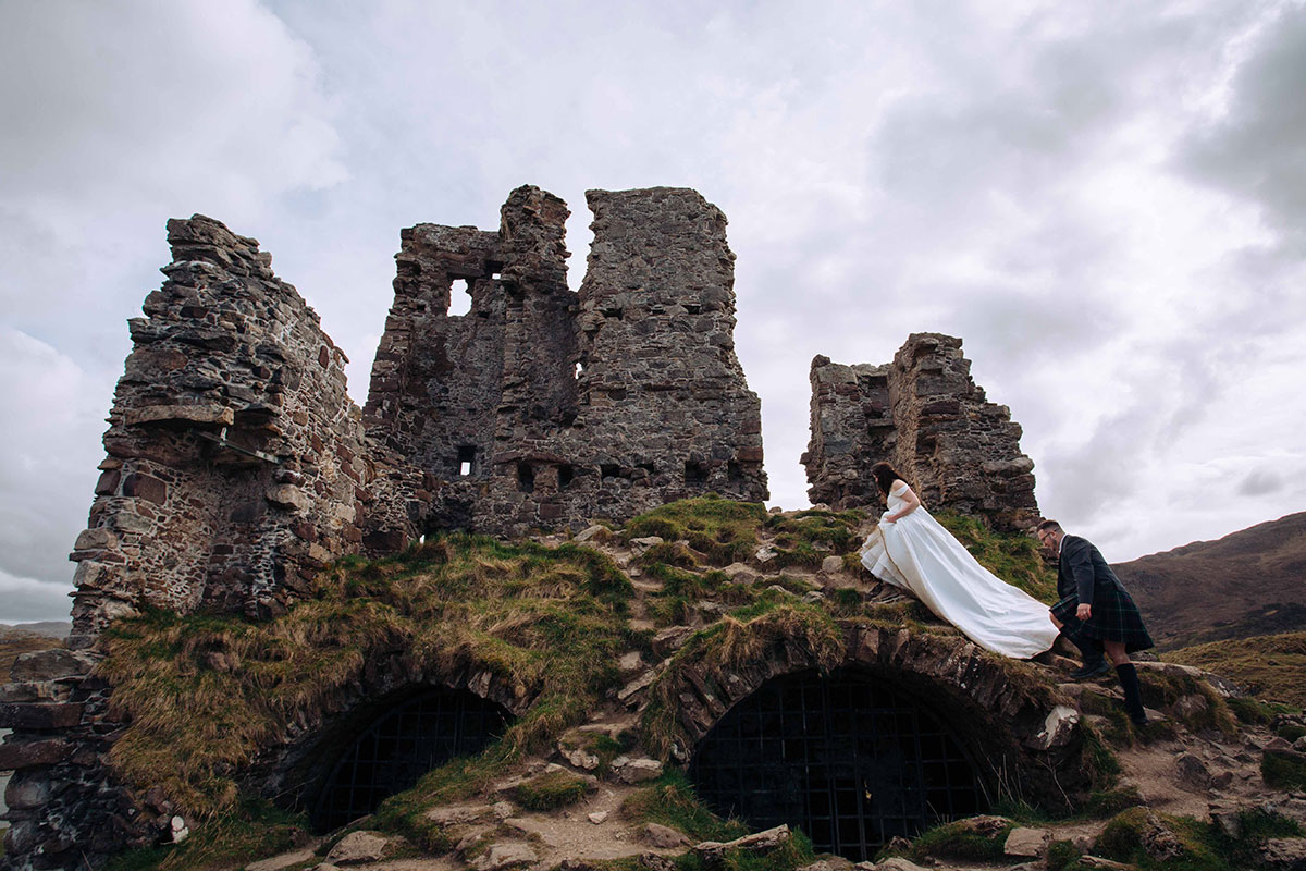 Bride and groom climb near the ruins of Ardvreck Castle for wedding portraits after their Achnahaird Bay ceremony.