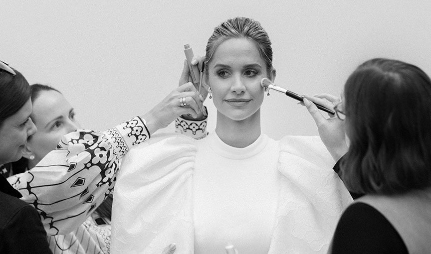 Bride smiling while multiple artists apply makeup during final touch-ups.