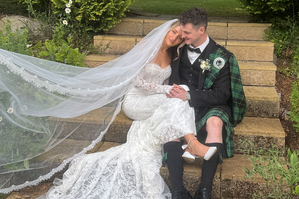 a bride and groom sitting on stone stairs in a garden setting