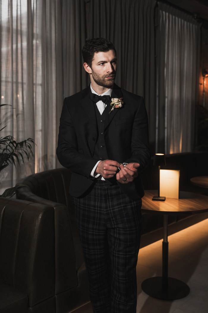 a groom wearing a dark tartan trews outfit from McCalls in a dark room at the Exchange in Glasgow