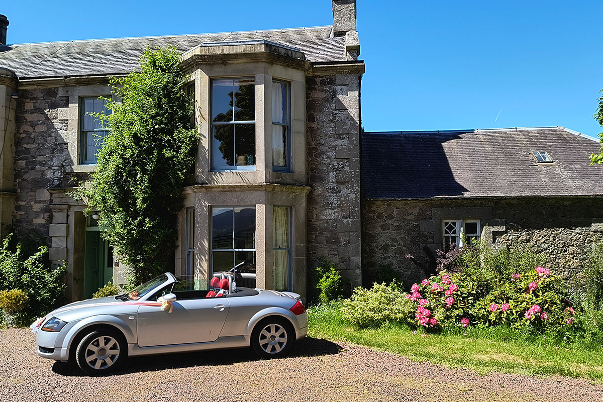 Stone farmhouse exterior at Cormiston Farm with gravel drive and parked car on a sunny day